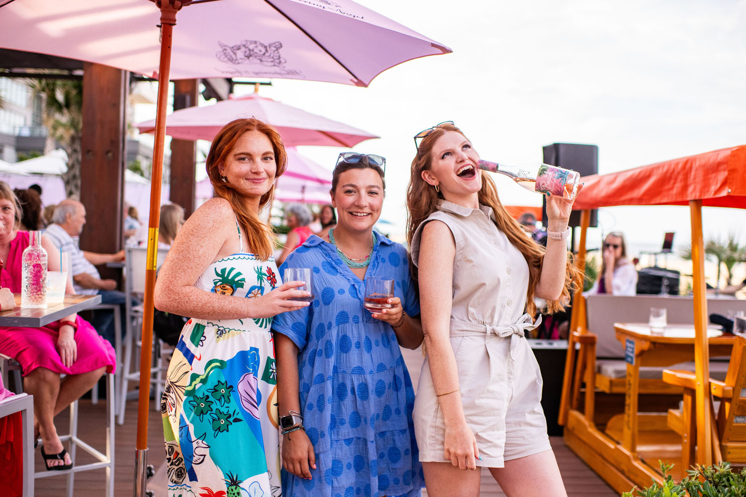 Three women holding drinks outside near the beach