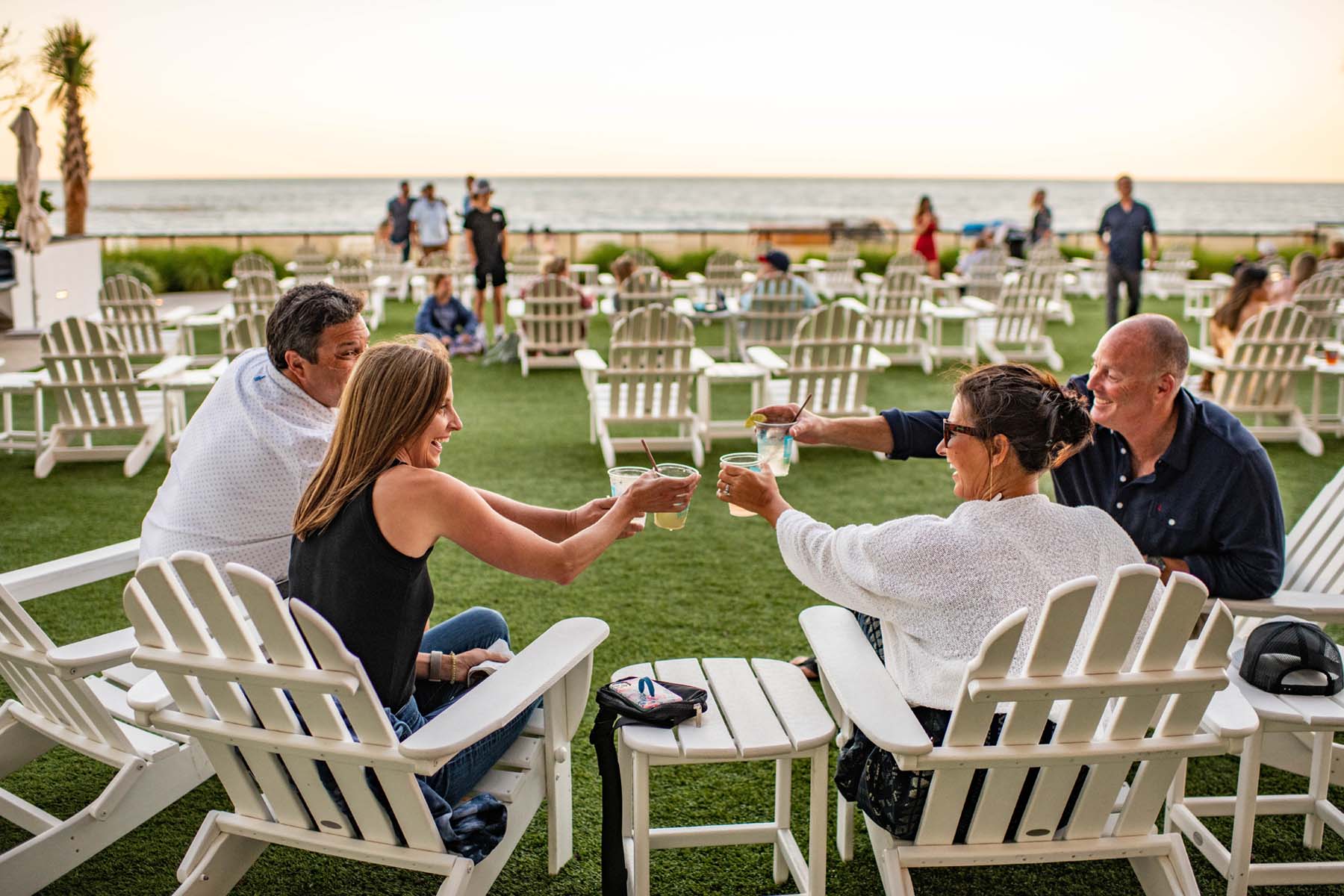 Four people sitting in chairs on a lawn next to the ocean
